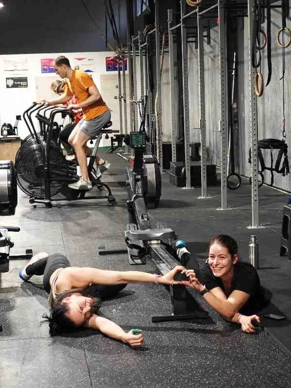Zwei Sportlerinnen formen nach dem Workout am Boden ein Herz mit den Händen