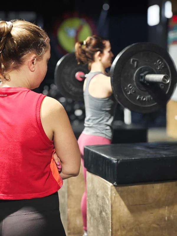 Zwei Sportlerinnen warten am Rack auf den nächsten Satz Kniebeugen